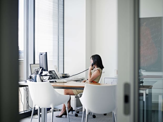 VoIP Tech Businesswoman sitting at desk in office talking on phone smiling