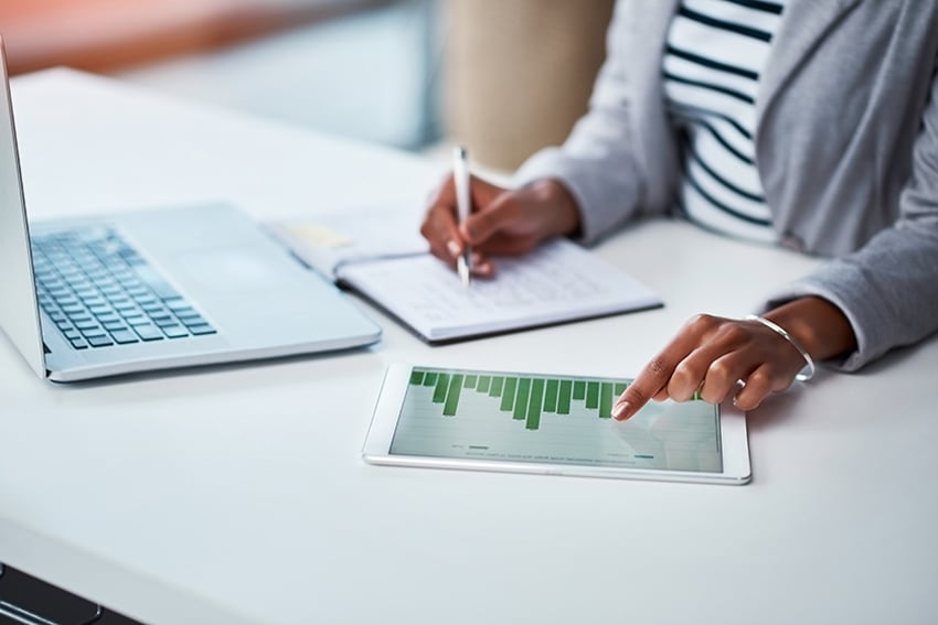 1041512864 Person, die Finanzinformationen von Diagramm und Laptop vor ihr aufschreibt