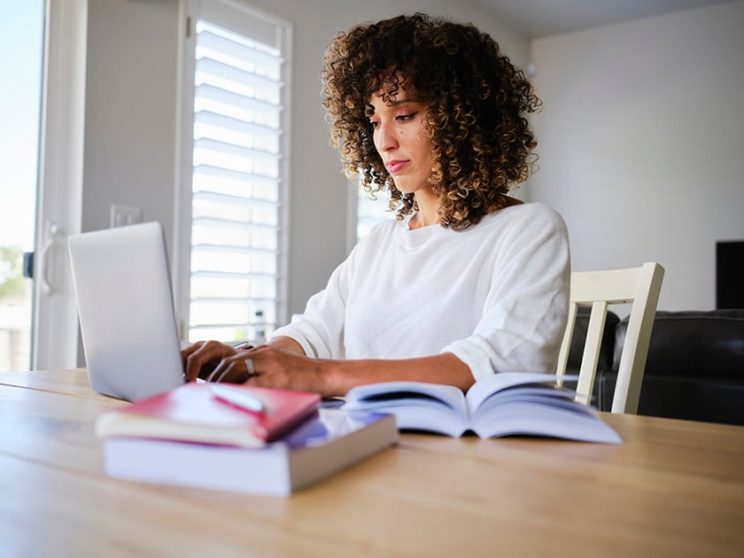 Schülerin mit geöffneten Schulbüchern, die auf einen Laptop-Computer schaut